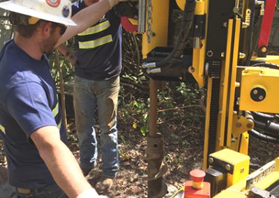 New, limited access rubber track drilling rig conducting soil sampling in tight quarters in dense brush.